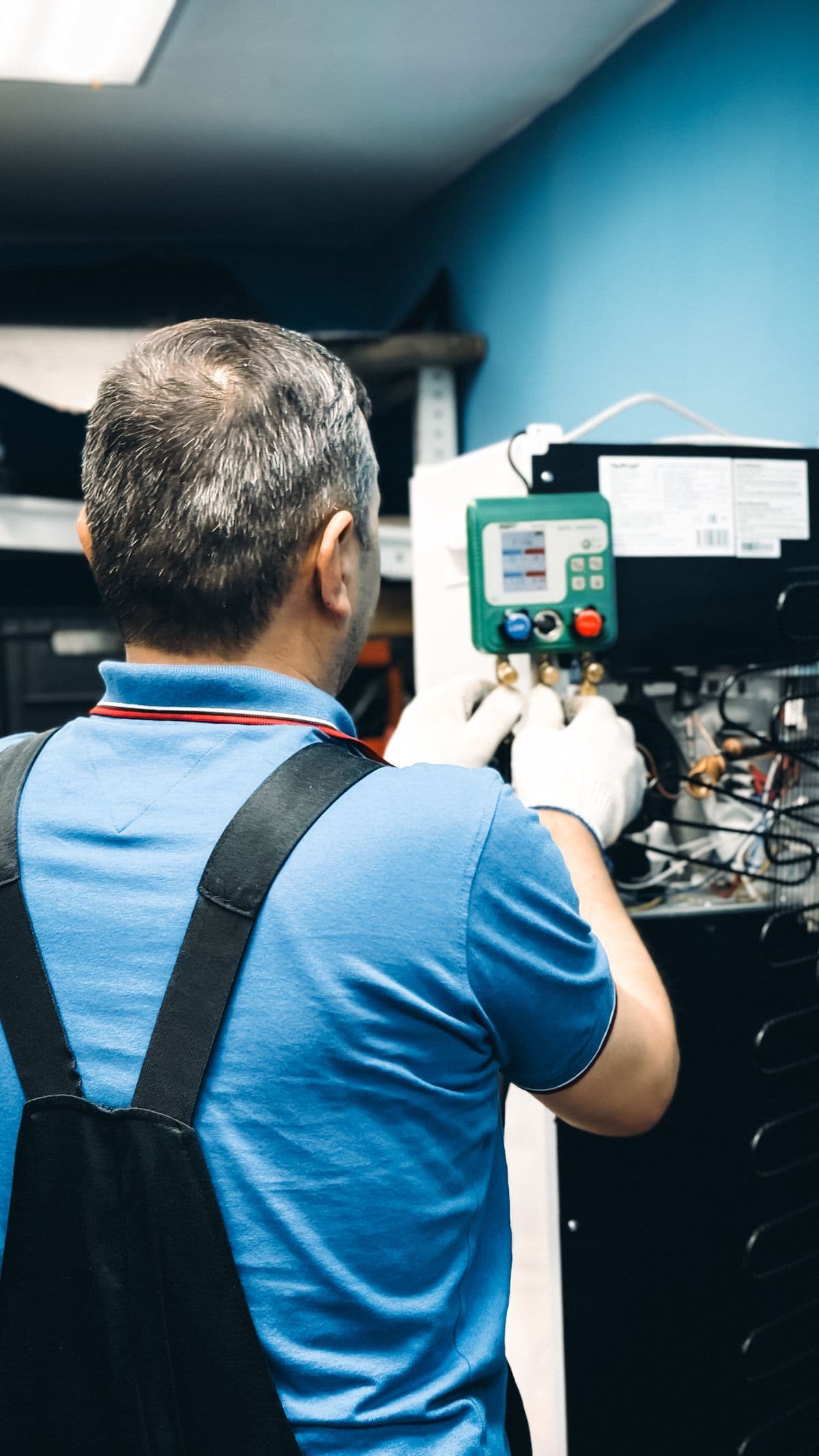 An HVAC technician connecting manifold gauges to an indoor air handler during an AC installation
