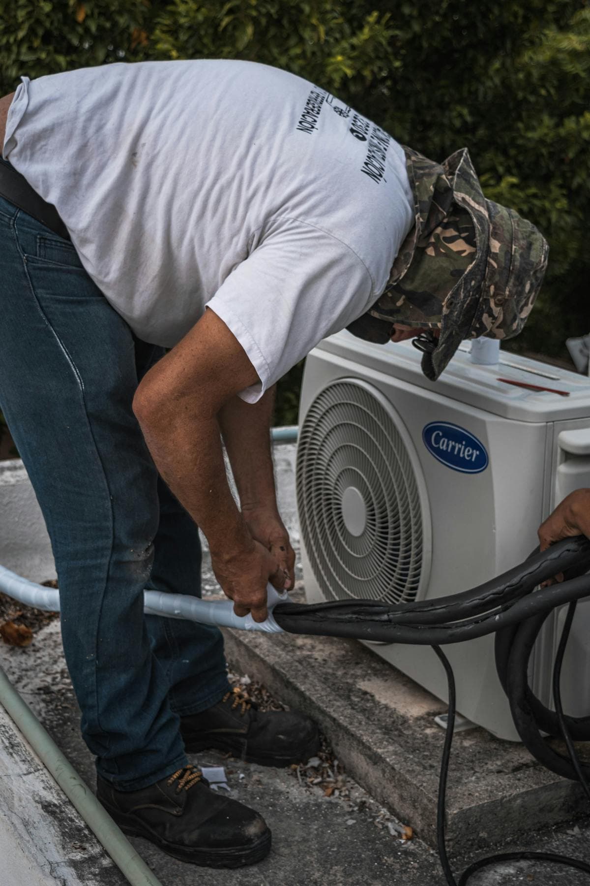 Technician servicing the line connections on a residential Carrier AC condenser during maintenance