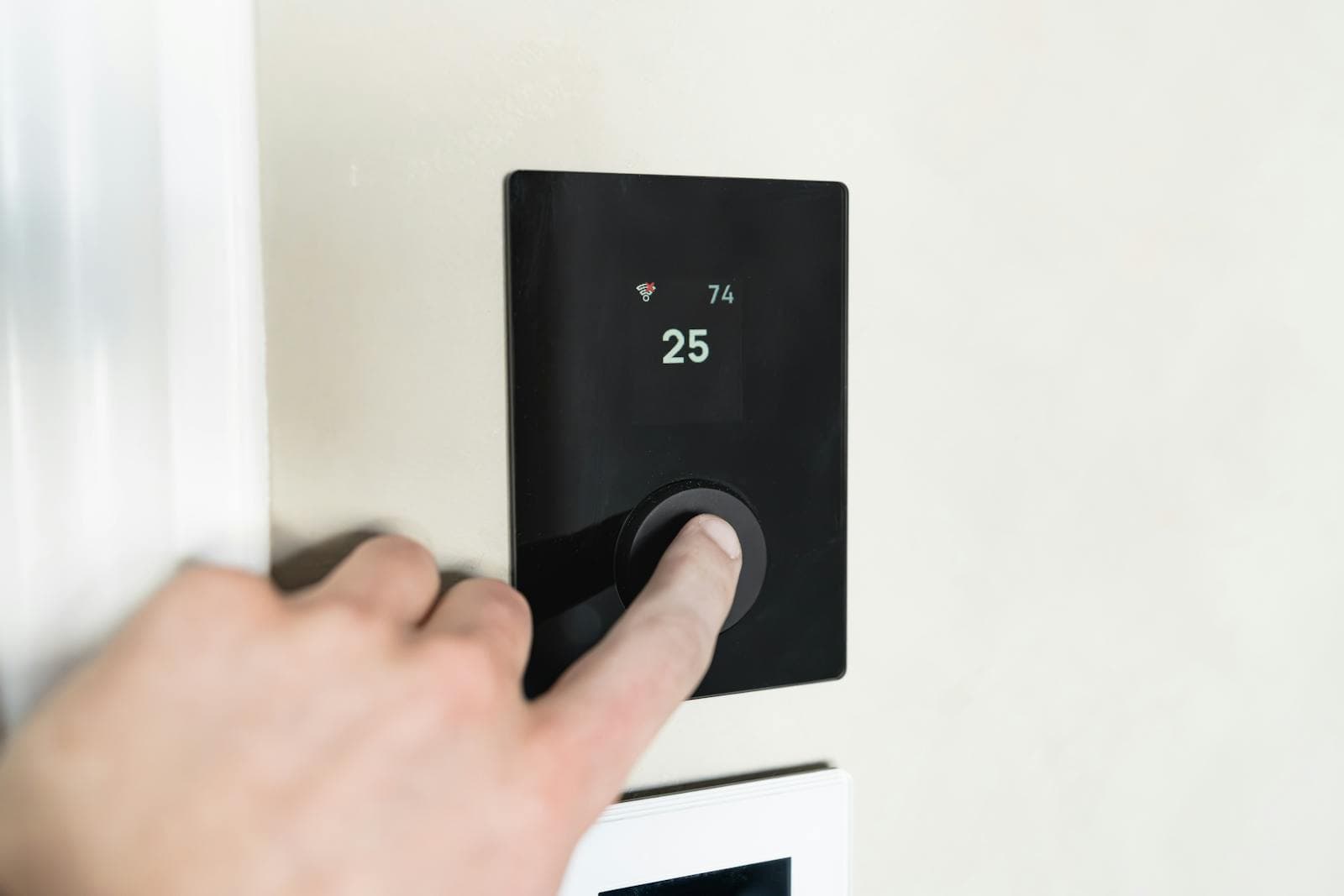 A person adjusting a sleek black Wi-Fi smart thermostat mounted on a home wall